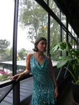 Vestido corto turquesa cubierto de lentejuelas brillantes, con escote en cascada, tirantes que se aten al cuello y volado en el ruedo.