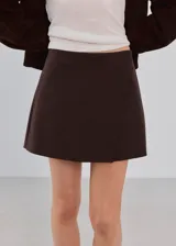 Minifalda marrón oscuro de corte recto, con diseño liso y cierre cruzado simulado.
