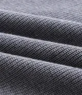 Suéter de punto de algodón con textura perlada, color gris melange. Presenta cuello polo con cierre de tres botones, manga larga y terminaciones acanaladas en puños y ruedo.