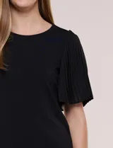 Blusa blanca con escote redondo y mangas cortas estilo mariposa confeccionadas en tela plisada translúcida.