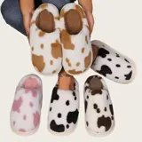 Pantuflas sin talón confeccionadas en algodón afelpado con estampado de vaca en tonos blanco y marrón, con suela de PVC.