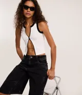 Musculosa blanca sin mangas de tejido seamless con cremallera frontal vertical y ribetes negros en contraste en el cuello y las sisas.