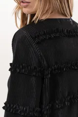Blusa negra plisada de manga larga con detalles de volados horizontales en el frente y las mangas.