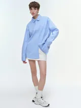 Camisa oversize de popelina de algodón con diseño de rayas verticales, cuello clásico, cierre frontal con botones, manga larga con puños anchos y bolsillo aplicado en el pecho.