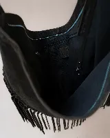 Cartera tipo hobo de gamuza color beige, con diseño amplio y detalle de flecos largos en todo el contorno. Cuenta con un asa superior con pespuntes artesanales y cierre principal.