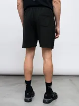 Bermuda de felpa negra con efecto lavado, corte recto y cordón ajustable en la cintura. Presenta un panel vertical en la parte delantera de cada pierna y el logo Umbro bordado en blanco en el muslo izquierdo.