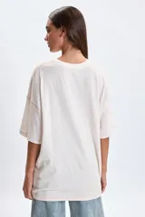 Remera de corte oversize color crudo, con cuello redondo y mangas cortas. Presenta una estampa frontal de flores en tonos violeta y el texto 'FLORAL GALLERY' en la parte inferior.