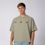 Remera boxy de corte cuadrado y hombro caído, color verde militar, con cuello redondo y diseño minimalista en el pecho que incluye texto y el logo en el centro.
