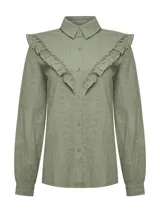 Blusa verde de algodón orgánico con cuello camisero, manga larga y cierre frontal de botones. Presenta volantes bordados que recorren el frente, la espalda y las sisas, además de detalles bordados en toda la prenda.