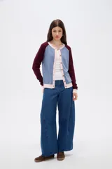 Cardigan de punto con diseño color block, presenta cuerpo en color celeste, mangas en color bordó y detalles de botones y bordes en color rosado. Posee cuello redondo y mangas largas.