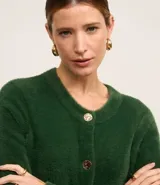 Cardigan de punto verde oscuro, con textura afelpada y cuello redondo. Cierre frontal con botones dorados y mangas largas con puños largos.