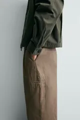 Pantalón de corte baggy fit confeccionado en tejido de algodón con estructura diagonal y efecto lavado. Presenta cintura con pliegues frontales, bolsillos laterales, bolsillos traseros de vivo y un bolsillo lateral adicional con doble vivo en la pernera. Cierre frontal con cremallera y botón.