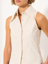 Camisa sin mangas confeccionada en tela de punto lisa, color crema, de corte regular. Lleva cartera con broches JCH y pinzas que entallan la prenda.