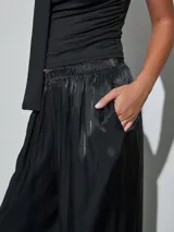 Pantalón negro de satén, de corte fluido y estilo bombacho, con cintura elástica y puños fruncidos en los tobillos con detalle de lazo.