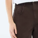 Pantalón de jean color marrón con corte globo, tiro alto y diseño de pierna ancha. Presenta costuras laterales marcadas y cierre frontal con botón y cremallera.