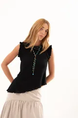 Blusa negra sin mangas con textura arrugada, cuello redondo y detalle de volados en los hombros. Presenta un corte asimétrico en el ruedo.