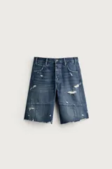 Bermuda baggy fit confeccionada en denim de algodón con lavado azul y efecto rotos en toda la prenda. Presenta diseño de cinco bolsillos, detalles de costuras en las perneras, bajo acabado irregular y cierre frontal con cremallera y botón.