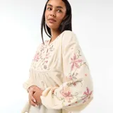 Blusa de color beige con cuello en V, mangas largas abullonadas con puños elásticos y bordados florales en el pecho y las mangas.