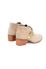 Bota corta de cuero gamuzado color avena, con taco fachetado efecto madera de 5 cm, punta redondeada y detalle de hebilla dorada lateral.