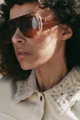 Chaqueta estilo safari color beige, con cuello de solapa tejido en crochet, manga larga, bolsillos delanteros con solapa y cintura ajustable con cordones. Cierre frontal con botones metálicos a presión.