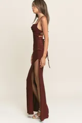 Vestido largo de fiesta confeccionado en tela lurex color bordó. Presenta un escote recto con breteles finos, corte ajustado al cuerpo y una abertura lateral profunda en la falda.