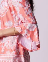 Blusa color salmón con estampado floral blanco, cuello redondo con abertura y mangas 3/4 acampanadas.