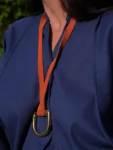 Collar con dije metálico en forma de estribo y tira de cuero color rojo. El dije es de color plateado.