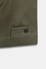 Pantalón de tiro alto en color verde militar, con corte barrel de pernera holgada que se estrecha hacia el tobillo. Presenta trabillas laterales ajustables en la cintura y en el bajo, bolsillos delanteros y cierre frontal con cremallera y botón.