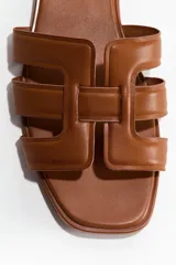 Sandalias planas de cuero marrón, con punta cuadrada y tiras superiores entrelazadas con diseño geométrico y acolchado.