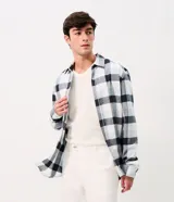 Camisa de corte comfort confeccionada en algodón, con cuello camisero, mangas largas y cierre frontal con botones. Presenta un estampado de cuadros en tonos celestes, blancos y azul marino.