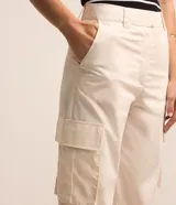 Pantalón recto color crema, confeccionado en tricolina, con cintura tipo sastreria, trabillas, cierre por botón y cremallera, y bolsillos cargo laterales.