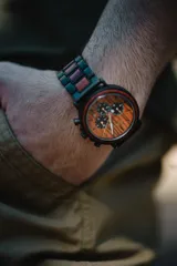 Reloj multifuncional para hombre, con caja de madera de sándalo rojo y acero inoxidable negro. La esfera es de madera de sándalo rojo con subdiales negros funcionales que ofrecen cronógrafo, indicador de 24 horas y fechador. La malla es de acero inoxidable negro con incrustaciones de madera de sándalo rojo.