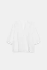 Camisa blanca de algodón con escote en pico, mangas por debajo del codo y detalles de bordados y encaje a tono en el pecho y las mangas.