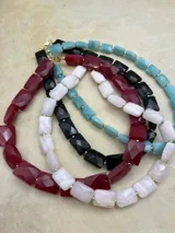 Collar corto de piedras facetadas rectangulares en rojo, blanco, negro y turquesa, con detalles dorados.