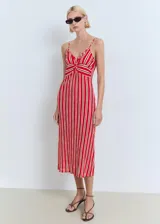 Vestido midi de tirantes finos ajustables, con escote en pico y detalle fruncido en la parte frontal. Presenta un diseño recto con estampado de rayas verticales en tonos rojo y blanco.