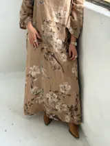 Vestido largo de lino color camel con estampado floral en tonos marrón y crudo, cuello drapeado y mangas largas holgadas.