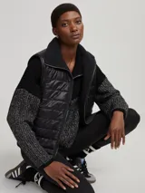 Chaleco negro capitoneado con cuello de piel sintética y cierre frontal con cremallera. Diseño sin mangas y corte recto.