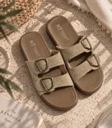 Sandalias planas de mujer con doble tira en tono mostaza de acabado gamuzado, sujetas por dos hebillas metálicas de estilo rústico y base marrón.