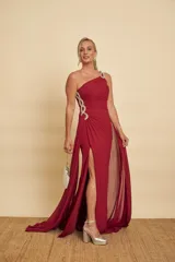 Vestido largo de fiesta color bordó, de un solo hombro, con detalles de pedrería en el tirante y fruncidos laterales. Cuenta con tajo pronunciado en la pierna y una capa larga vaporosa que cae desde el hombro.