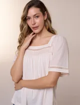 Blusa de corte holgado color marfil, confeccionada en mezcla de modal y algodón, con escote cuadrado y mangas cortas adornadas con detalles de puntilla calada.