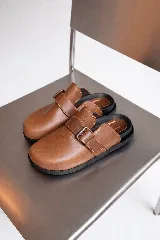Mules de cuero color suela con diseño de punta redondeada y tira ajustable con hebilla metálica sobre el empeine. Poseen una plantilla ergonómica y suela de goma negra.