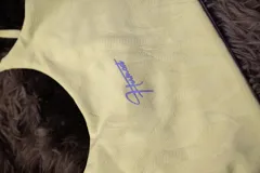 Top deportivo color amarillo claro con textura sutil y logo de la marca en color lila.