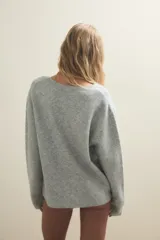 Cardigan de punto gris claro, con escote en V profundo, cierre frontal cruzado con botones y mangas largas holgadas.