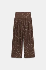 Pantalón de tiro alto con pernera ancha y diseño fluido. Presenta un estampado de lunares blancos sobre fondo marrón y detalle de frunces en la cintura.