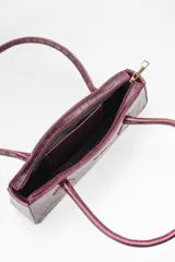 Cartera tipo baguette color negro con textura efecto cocodrilo, diseño alargado, doble asa de mano y cierre superior.