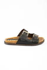 Sandalias de cuero negro con diseño de doble tira con hebillas metálicas doradas, plantilla de corcho y suela plana marrón.