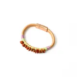 Pulsera rígida color dorado con cierre metálico y piedras irregulares color ladrillo. Decorada con hilo verde y detalles en hilo lila.