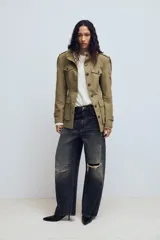 Chaqueta de estilo militar en color beige, con cuello subido, cierre frontal de botones, bolsillos de plastrón con solapa en el frente y detalle de hombreras con trabillas.