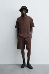 Camiseta de algodón de corte relajado (relaxed fit) color marrón oscuro, con cuello redondo y manga corta. Presenta una textura acanalada vertical tipo jacquard.