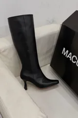 Botas altas de cuero negro, caña ajustada, punta fina y taco aguja de altura media.